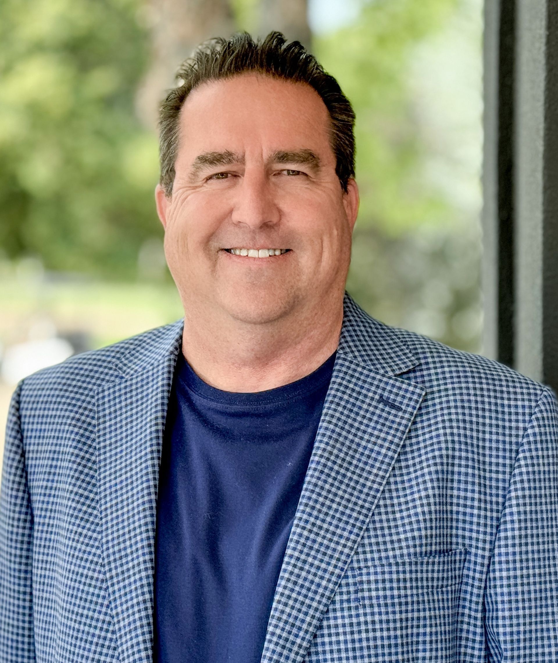 A man in a blue jacket and blue shirt is smiling for the camera.