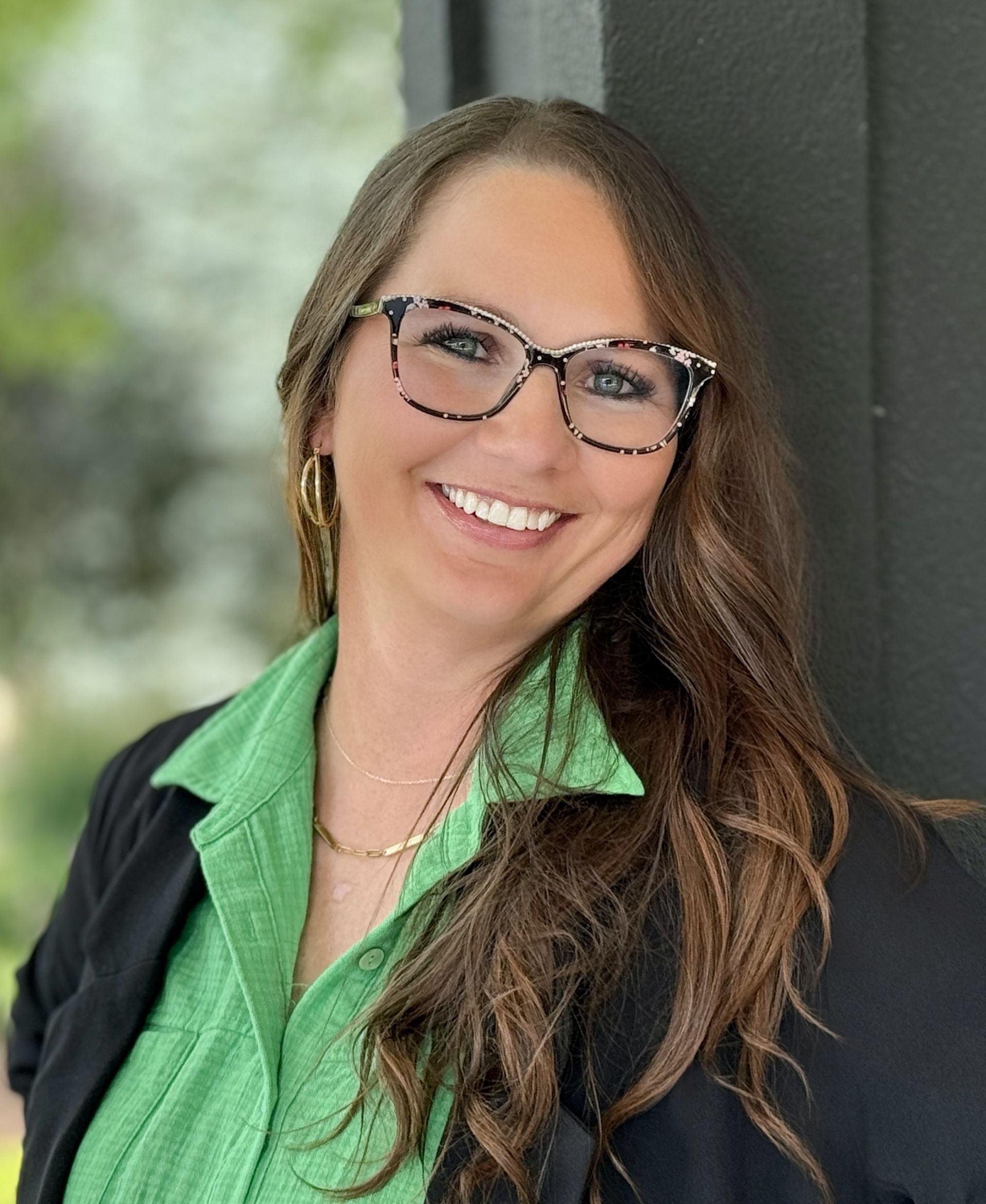 A woman wearing glasses and a green shirt is smiling for the camera.