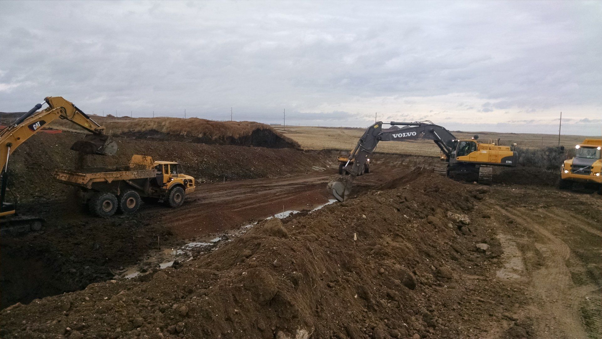 A group of construction vehicles are working on a dirt road.