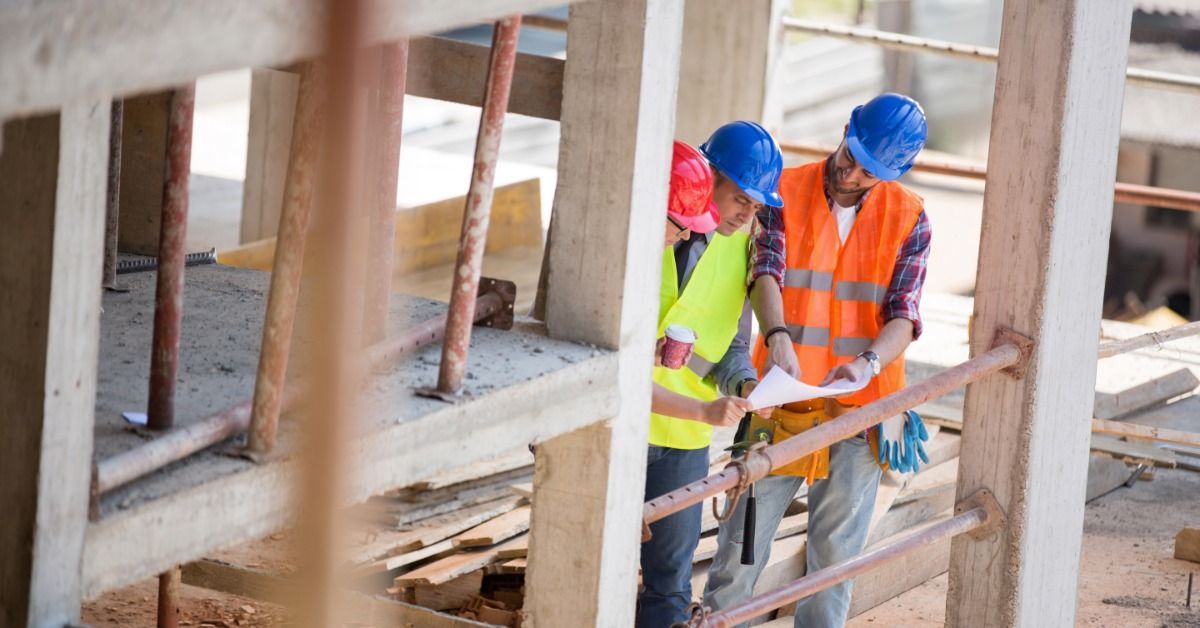 Three construction crew members standing on a job site. All three workers look at a small blueprint.