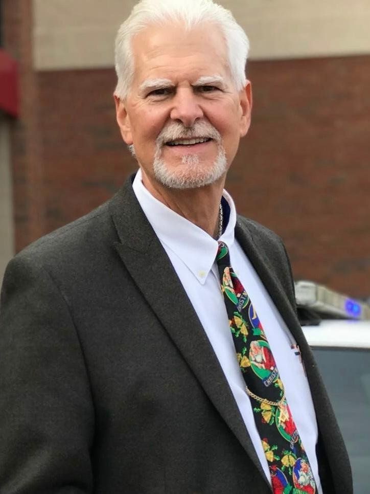 A man in a suit and tie is standing in front of a car.