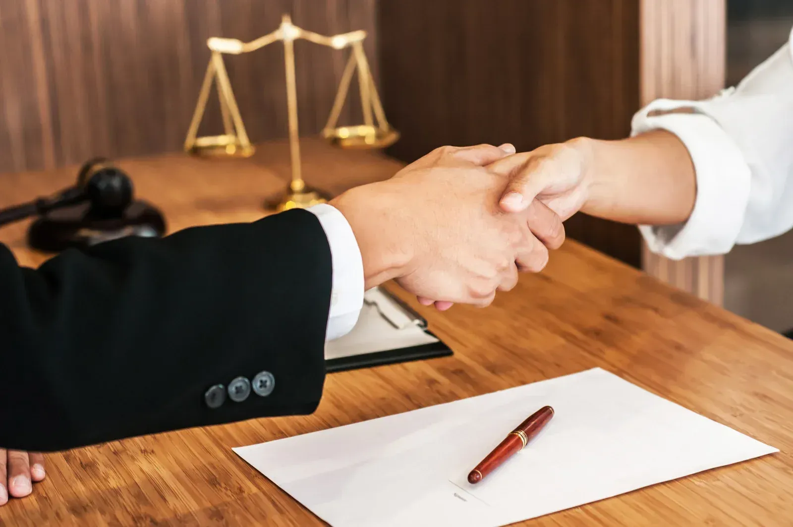 A lawyer is shaking hands with a client in front of a scale of justice.