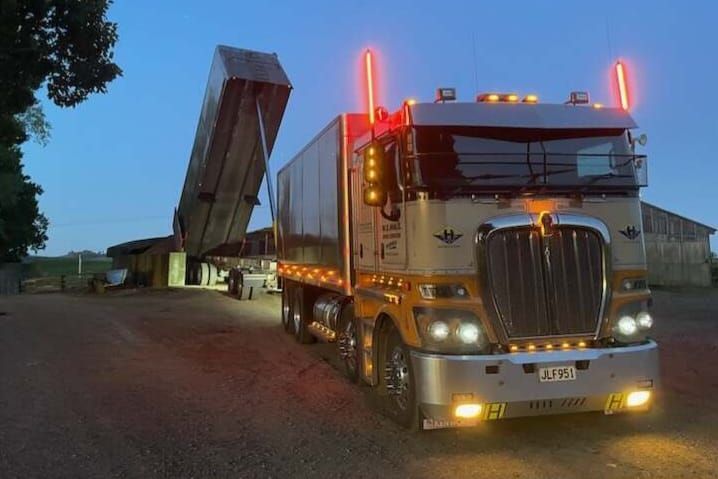A dump truck is dumping dirt on the side of a road.