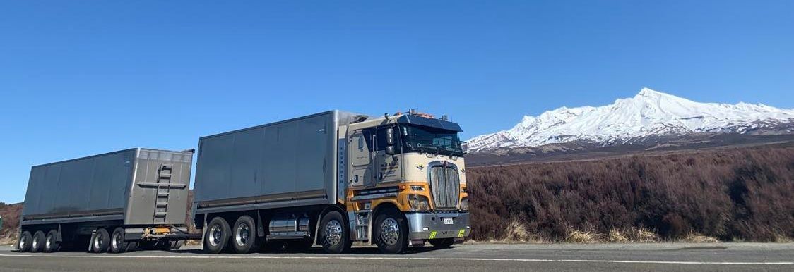 A red semi truck is driving down a highway at sunset.