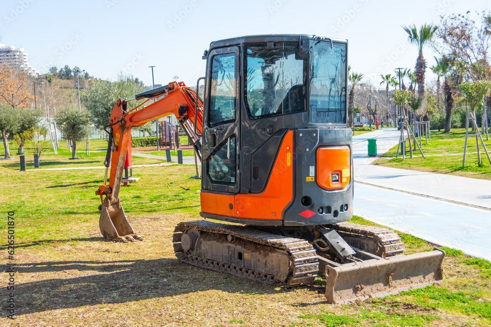 a small excavator is parked in the grass in a park
