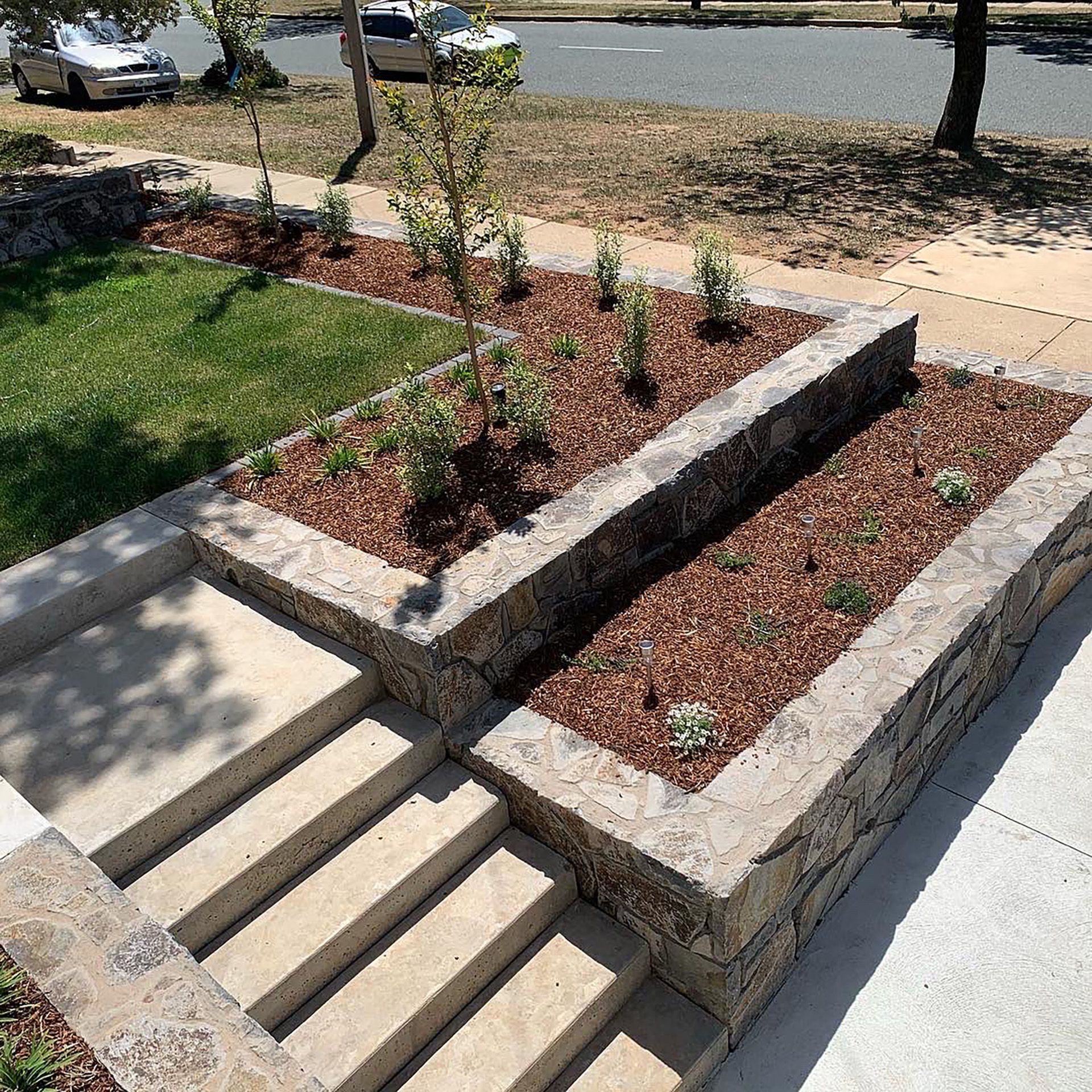 a set of stairs leading up to a garden with a car parked in the background