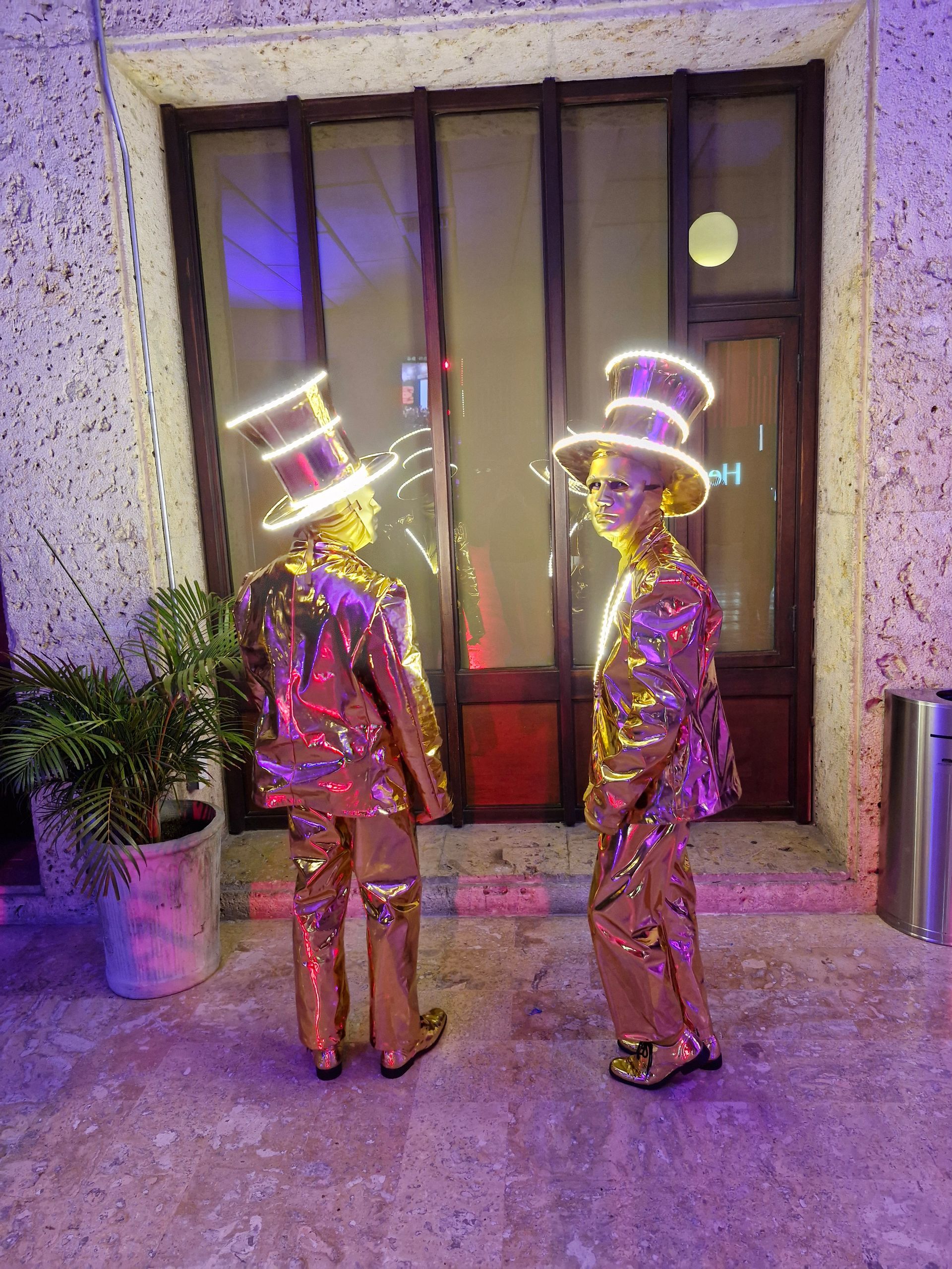 Dos hombres con trajes dorados y sombreros de copa están parados frente a un edificio.