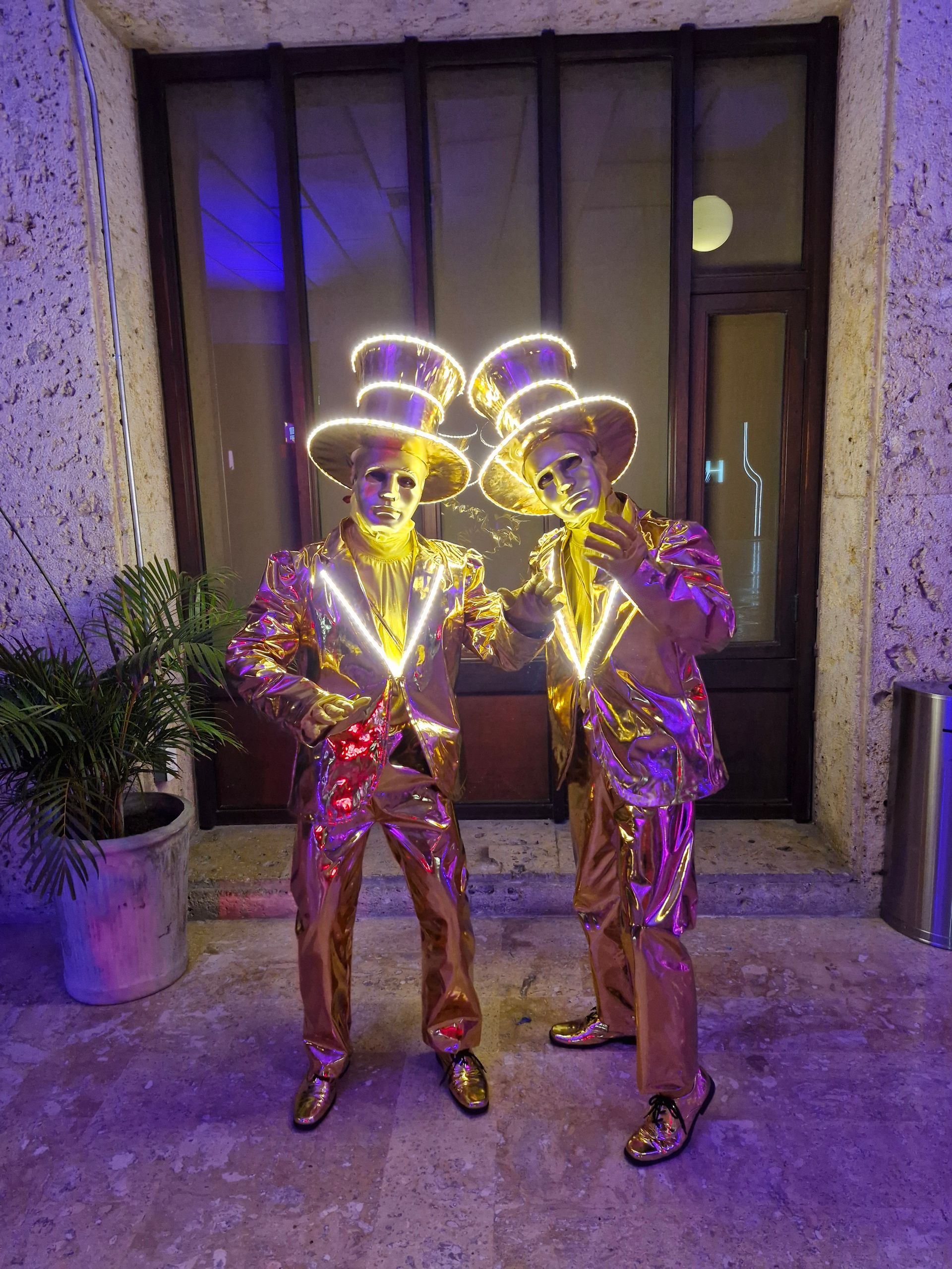 Dos hombres con trajes y sombreros dorados están parados uno al lado del otro frente a un edificio.