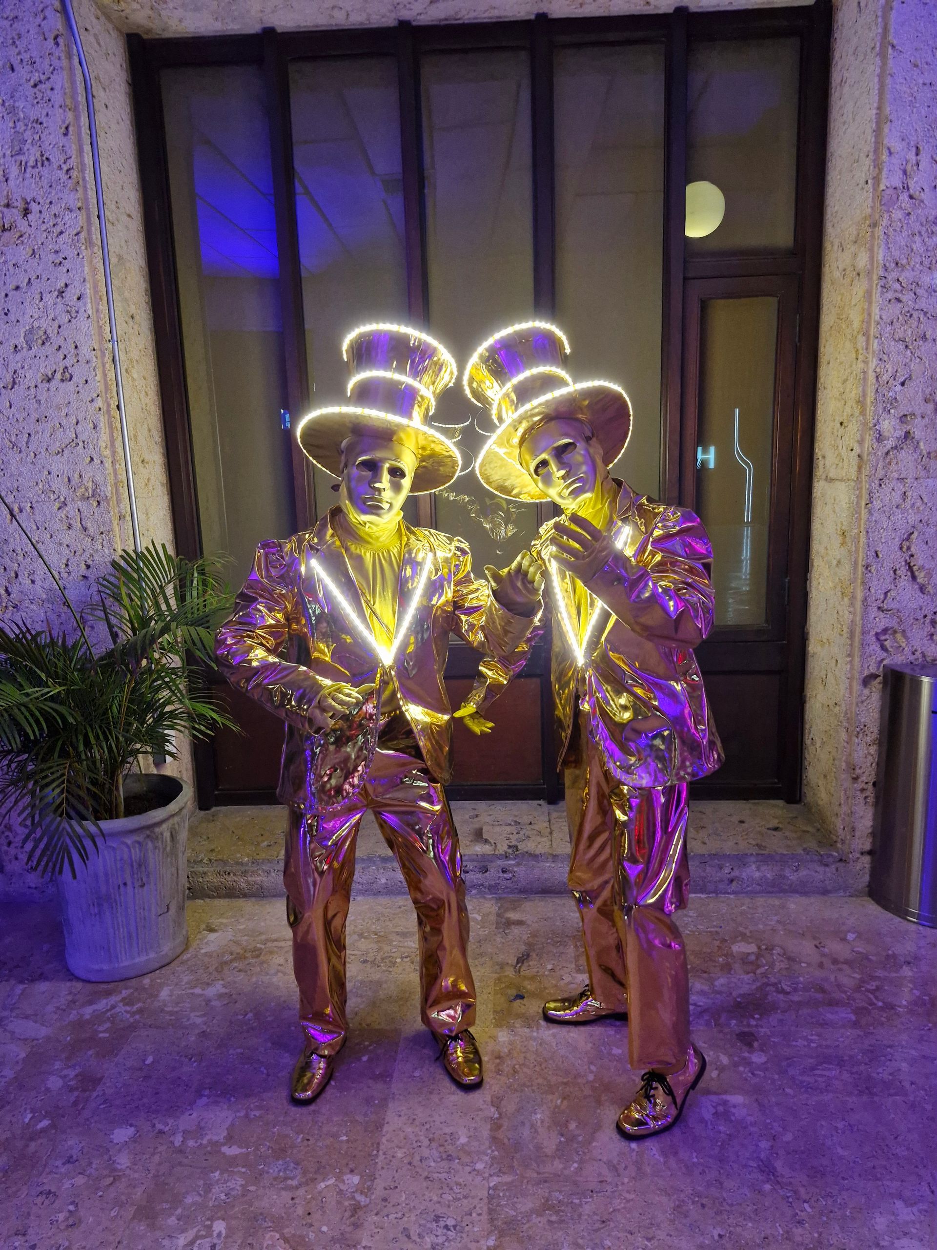 Dos hombres vestidos de oro están parados uno al lado del otro frente a un edificio.