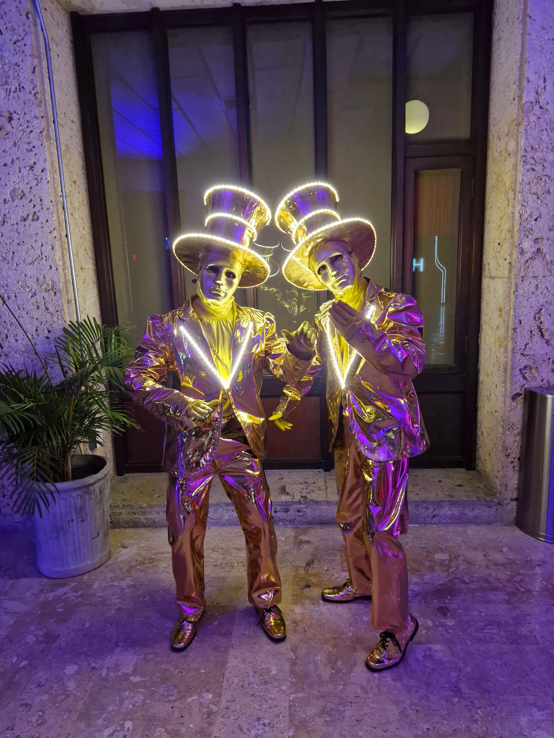 Dos hombres vestidos de oro están parados uno al lado del otro frente a un edificio.