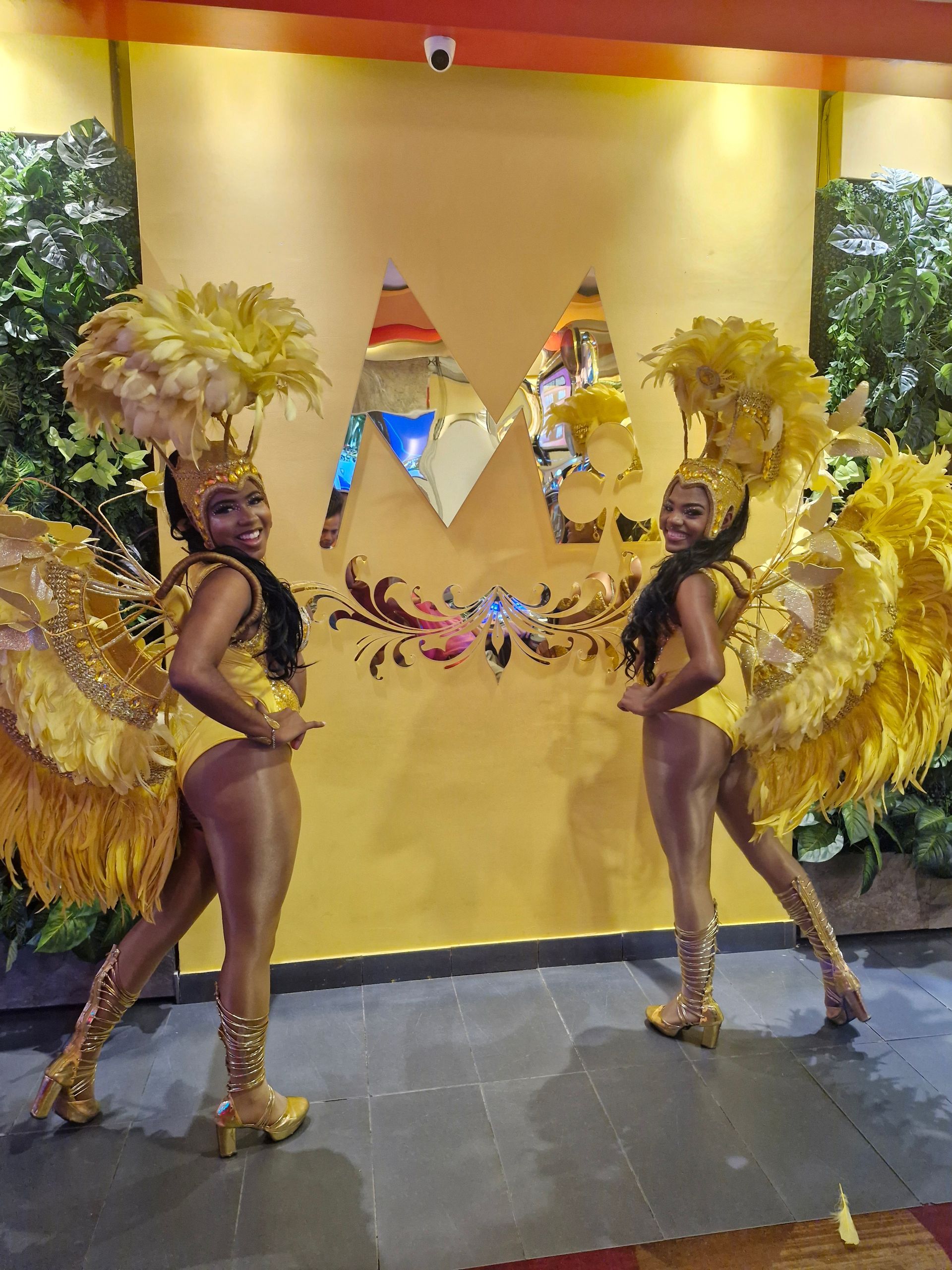 Dos mujeres disfrazadas de carnaval están paradas una al lado de la otra frente a una pared amarilla.