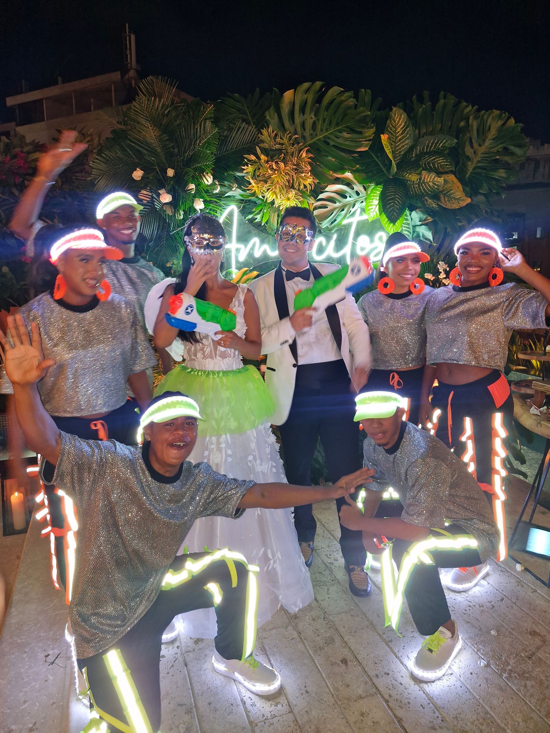 Una novia y un novio posan para una fotografía con bailarines que brillan en la oscuridad.