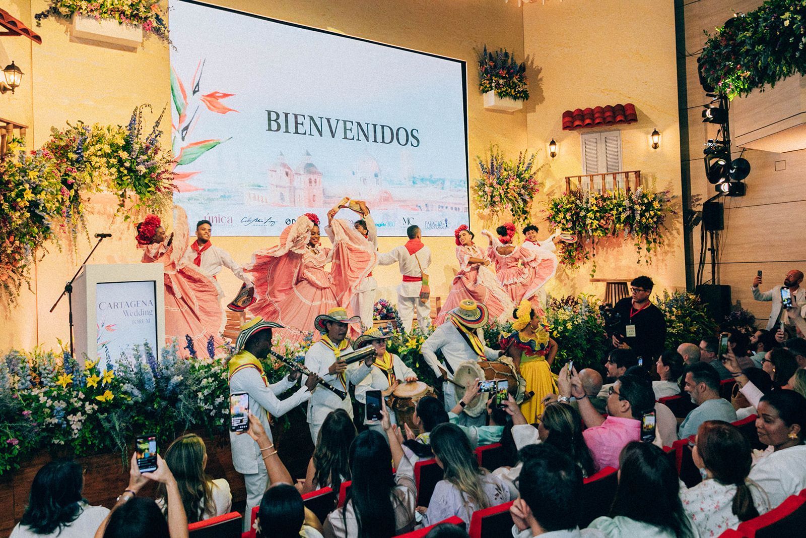 Un grupo de personas está sentado frente a una pantalla grande que dice bienvenidos