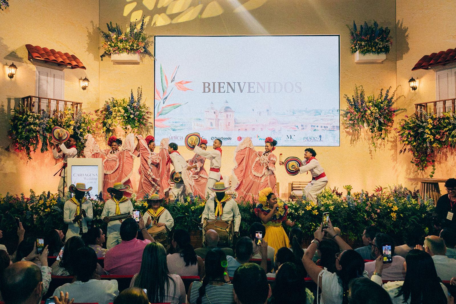 Un grupo de personas está sentada frente a una pantalla grande que dice bienvenidos.