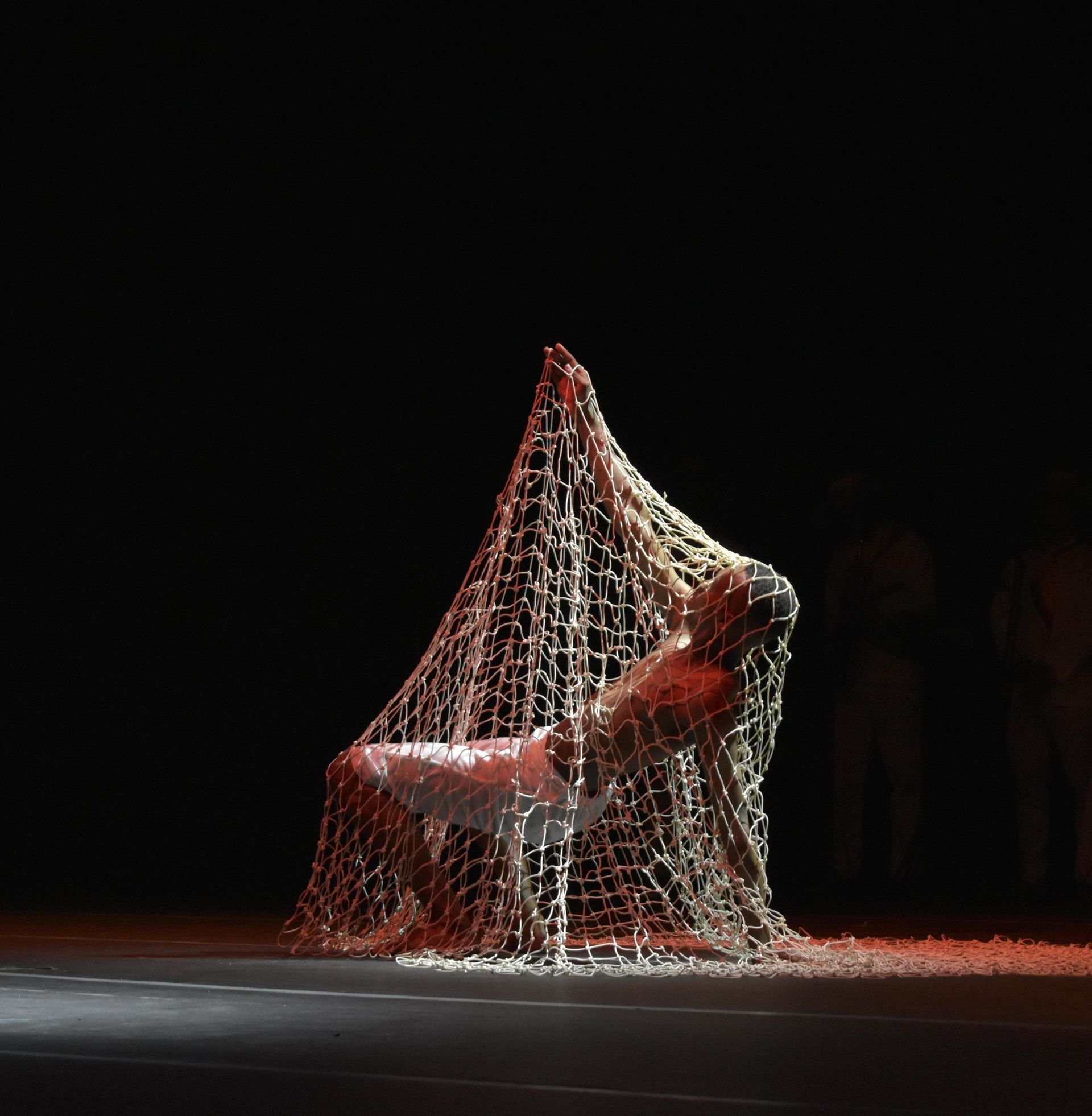 Una persona está envuelta en una red de pesca en un escenario. Kymbala. 