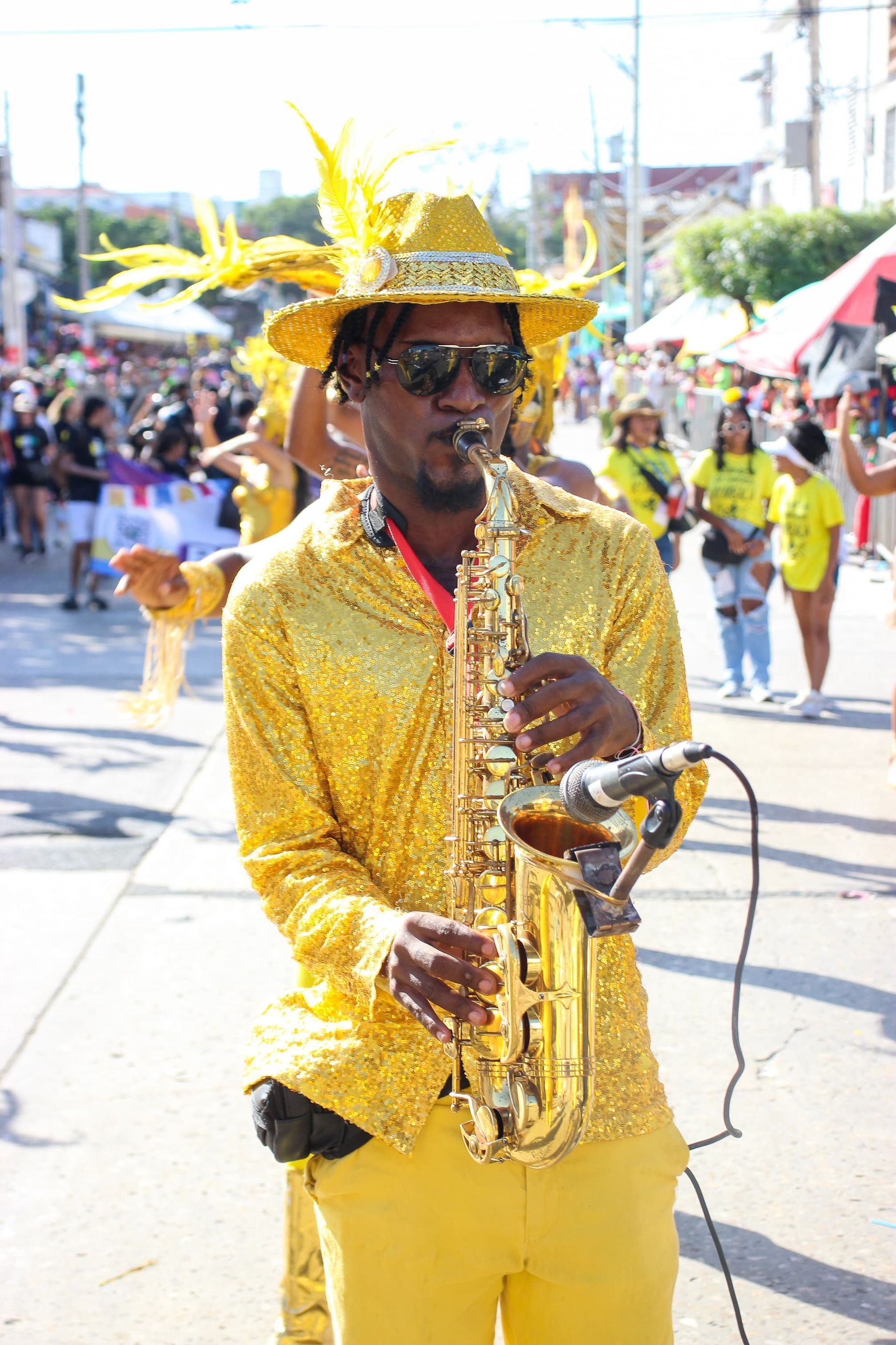 Un hombre vestido de amarillo toca un saxofón en un desfile.