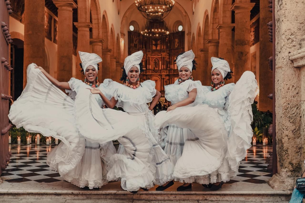 Un grupo de mujeres con vestidos blancos bailan frente a una iglesia.