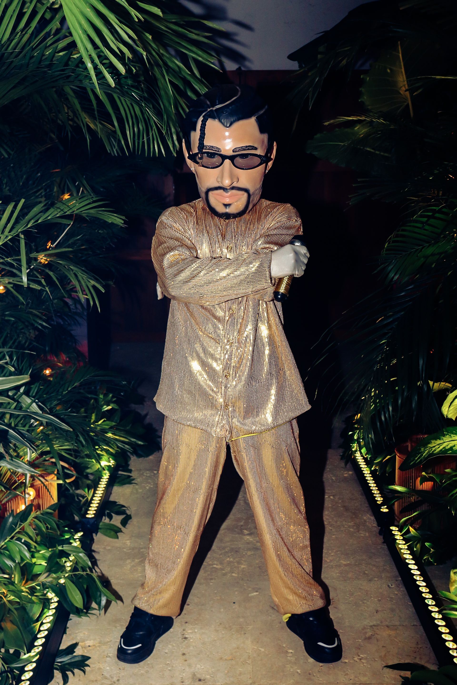 Una mascota con gafas y barba está de pie con los brazos cruzados.