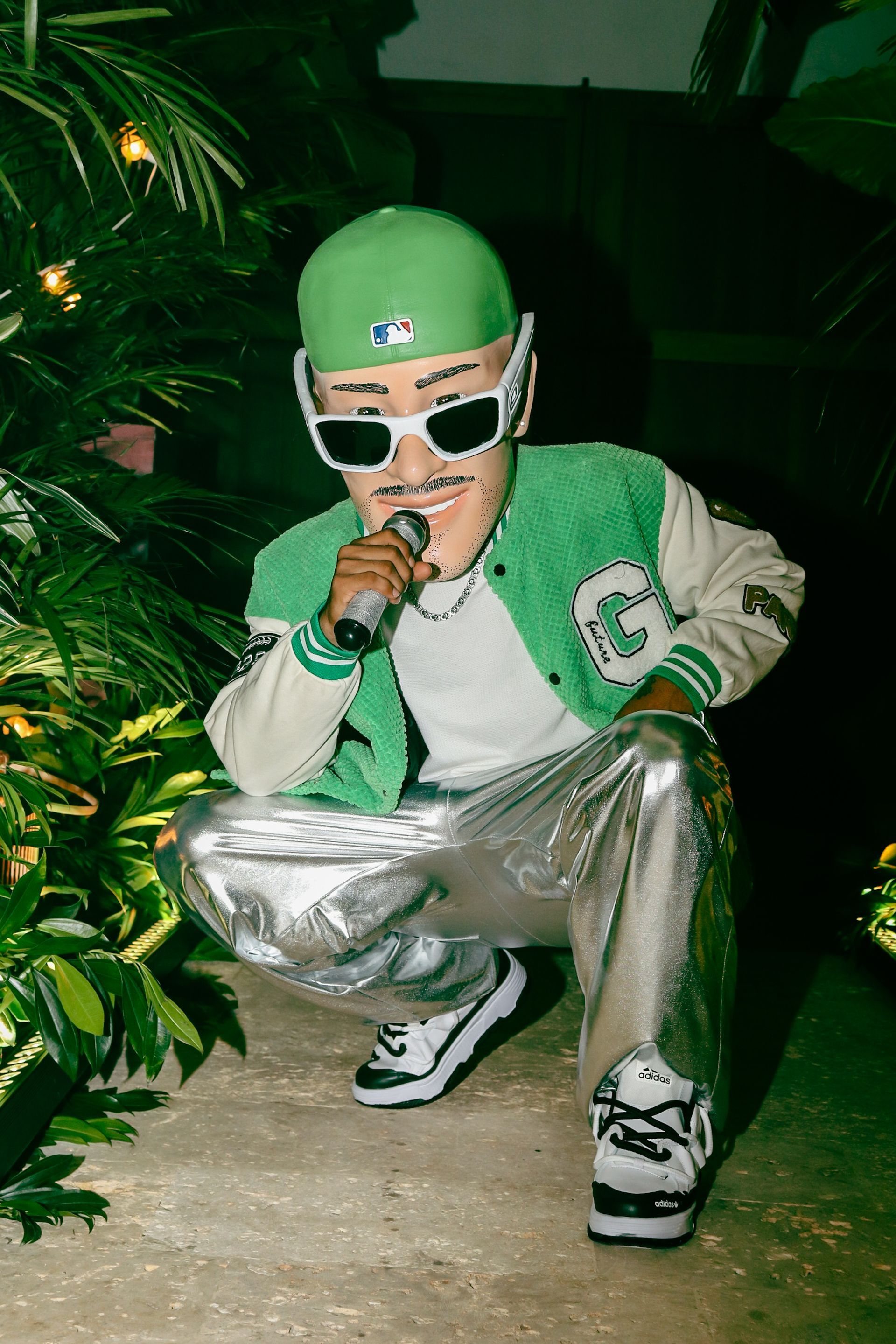 Un hombre que lleva un sombrero verde y gafas de sol está arrodillado y cantando frente a un micrófono.