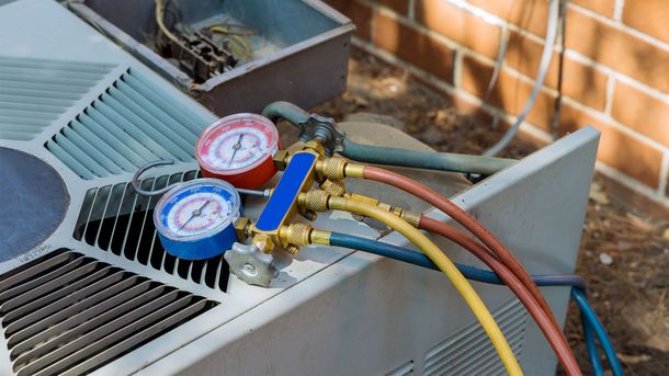 A HVAC manifold gauge set with red, blue, and yellow hoses connected to an outdoor air conditioning unit.