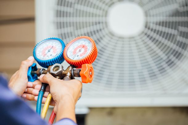A technician holding a dual-gauge manifold set to service an outdoor air conditioning unit.