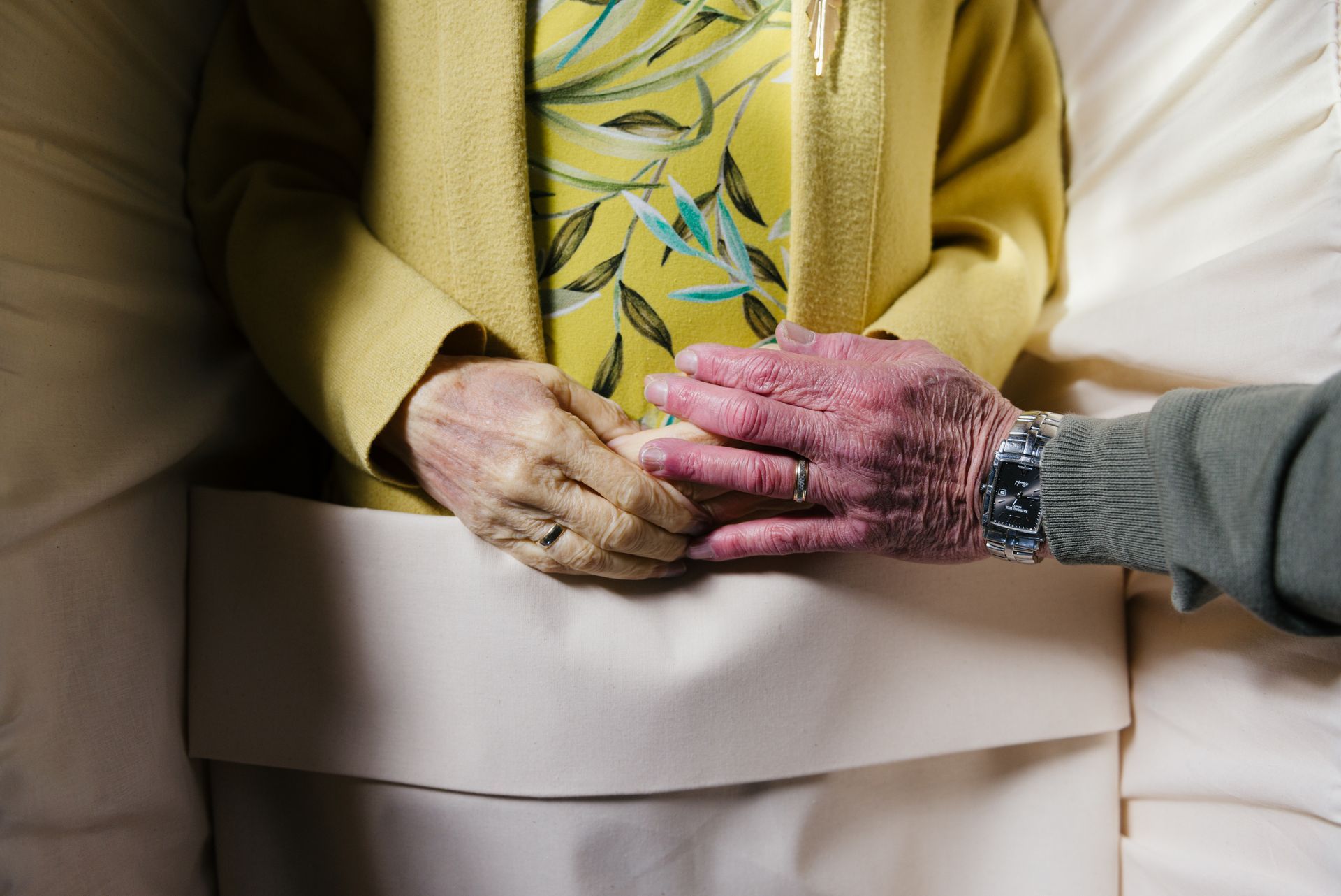 Een vrouw in een geel jasje houdt de hand van een andere vrouw vast.