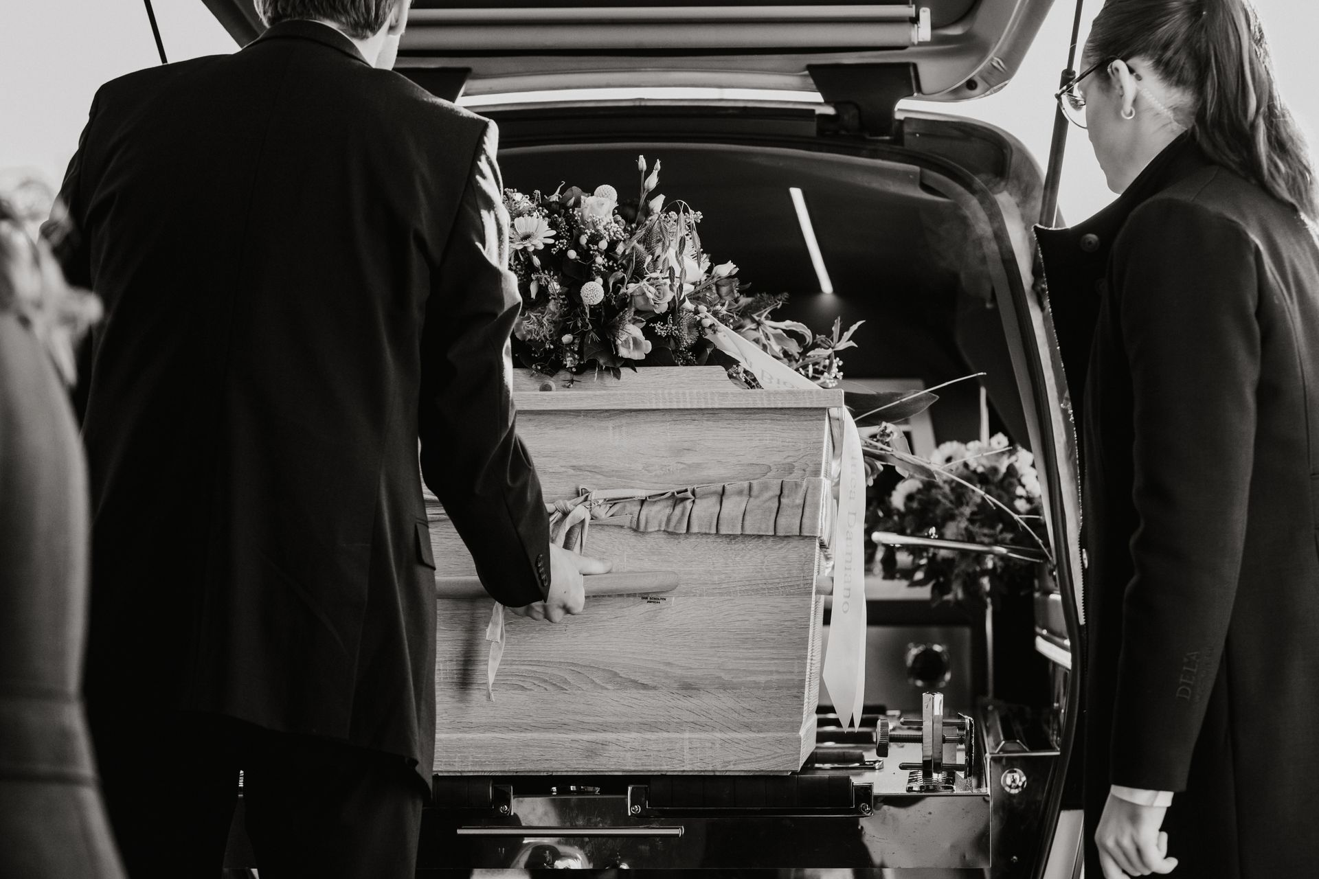 Een man en een vrouw dragen een doodskist in een auto.