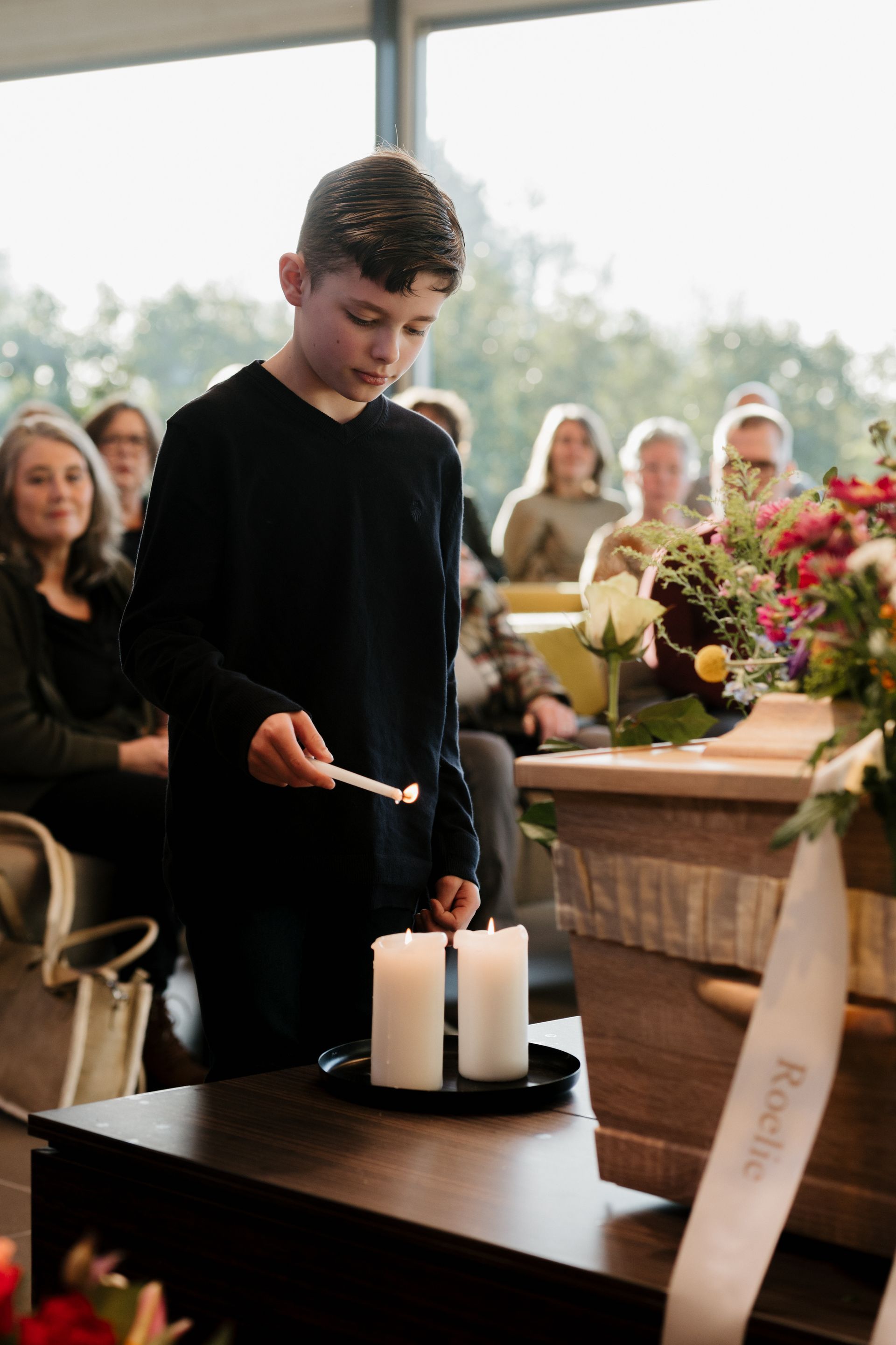 Een jonge jongen steekt een kaars aan op een begrafenis.