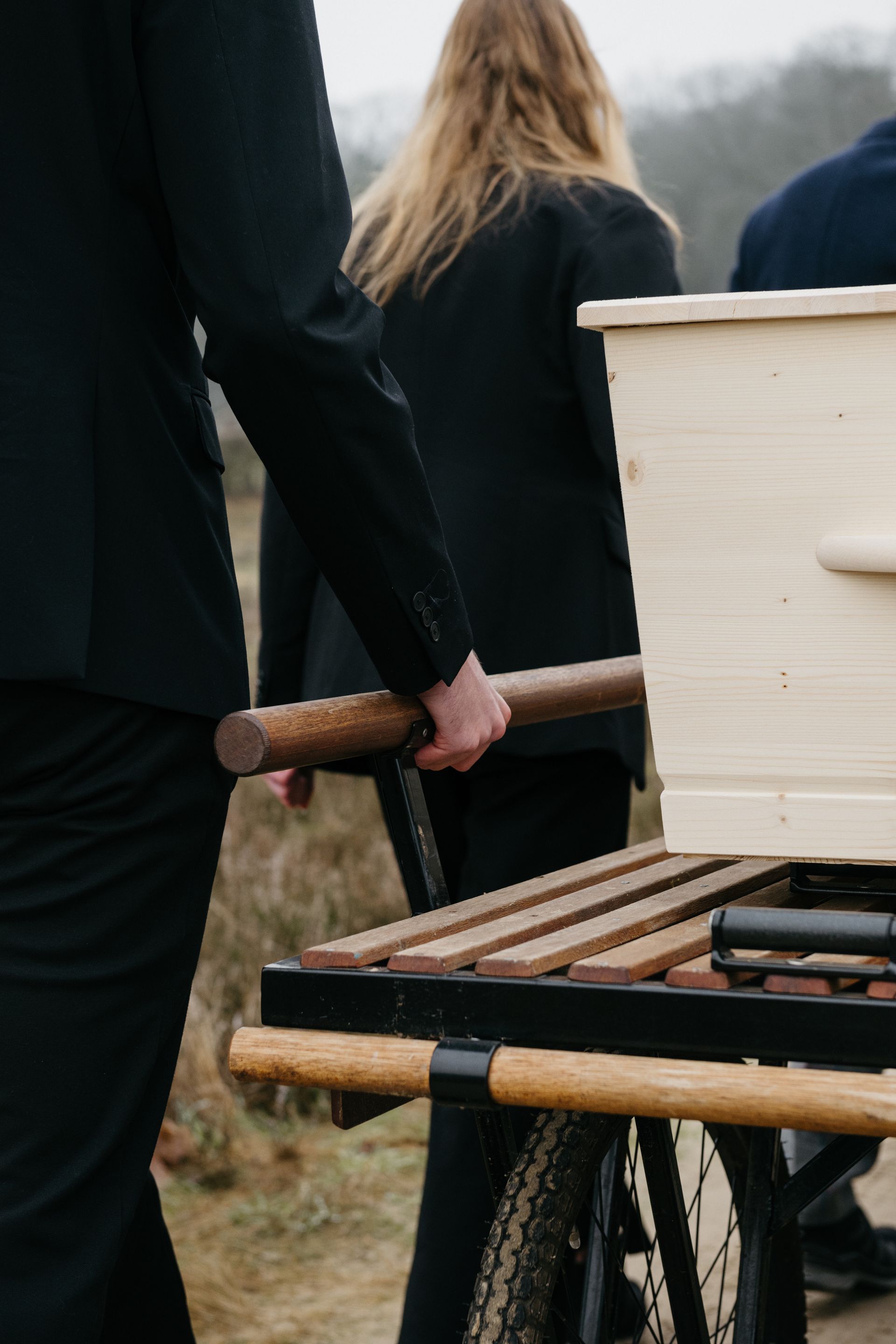 Een man duwt een houten doodskist op een kar.