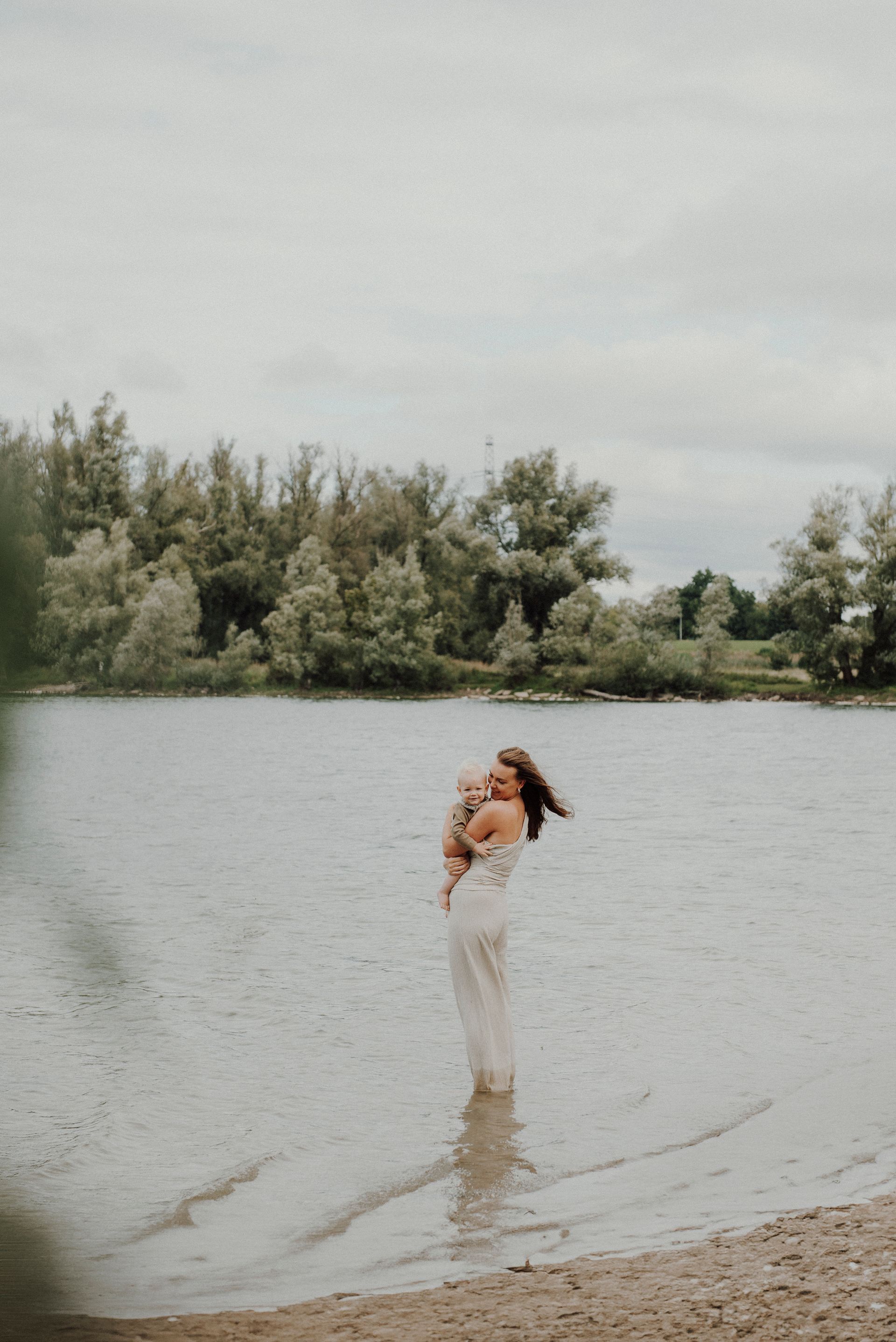 Een vrouw staat in het water met een baby in haar armen.