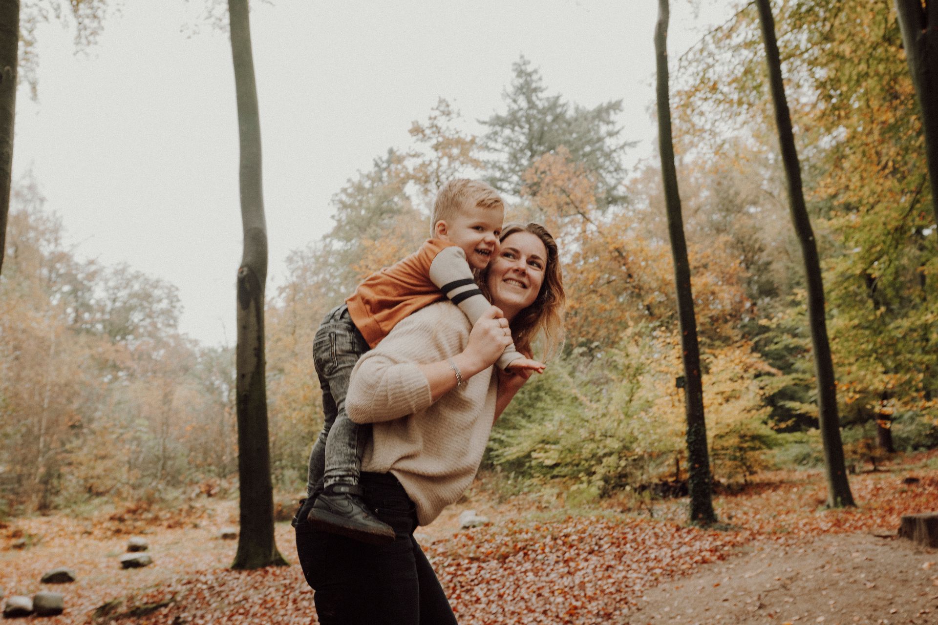 Een vrouw draagt een kind op haar rug in het bos.