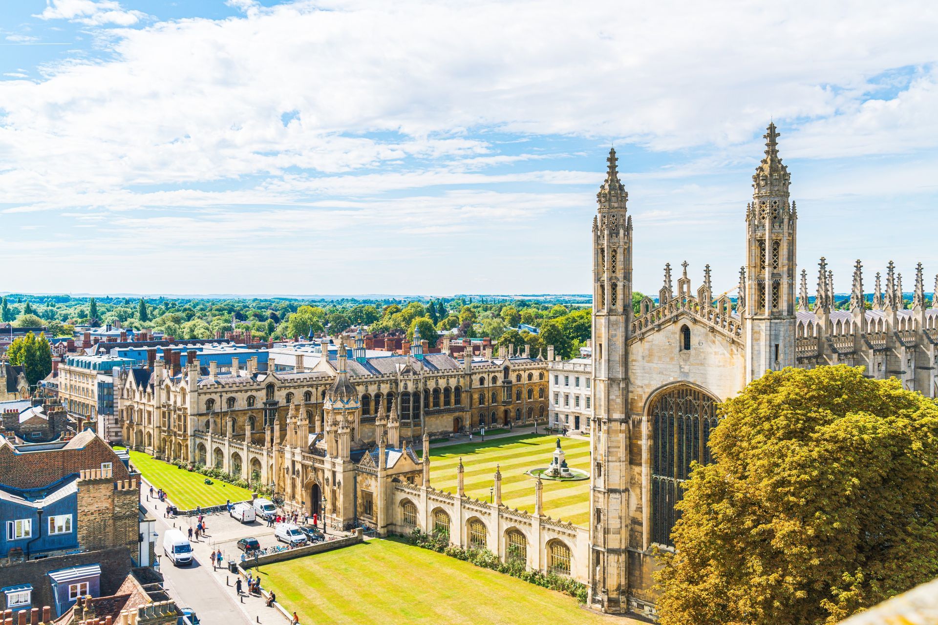 Aerial view of King's College Chapel, Cambridge, with green lawns, buildings, and a blue sky with clouds.