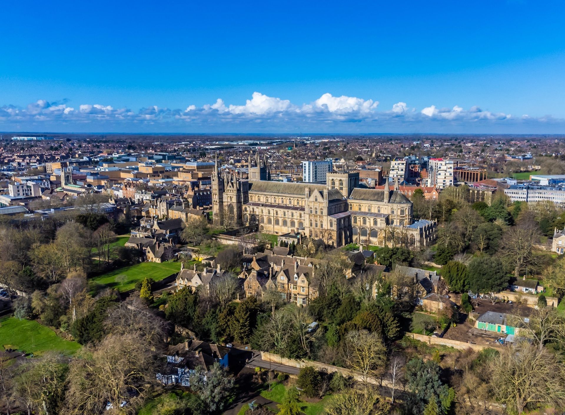 Aerial view of Peterborough Cathedral and surrounding town under a clear blue sky.