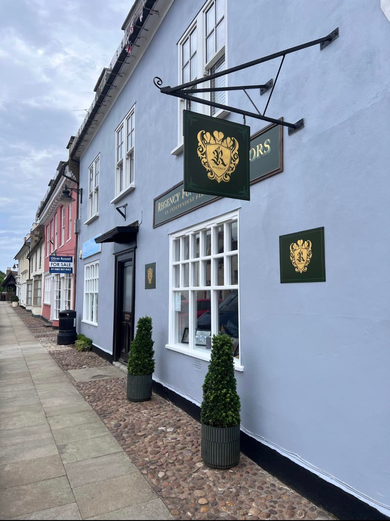 Blue storefront with a lion emblem sign. Other colorful buildings line the street.