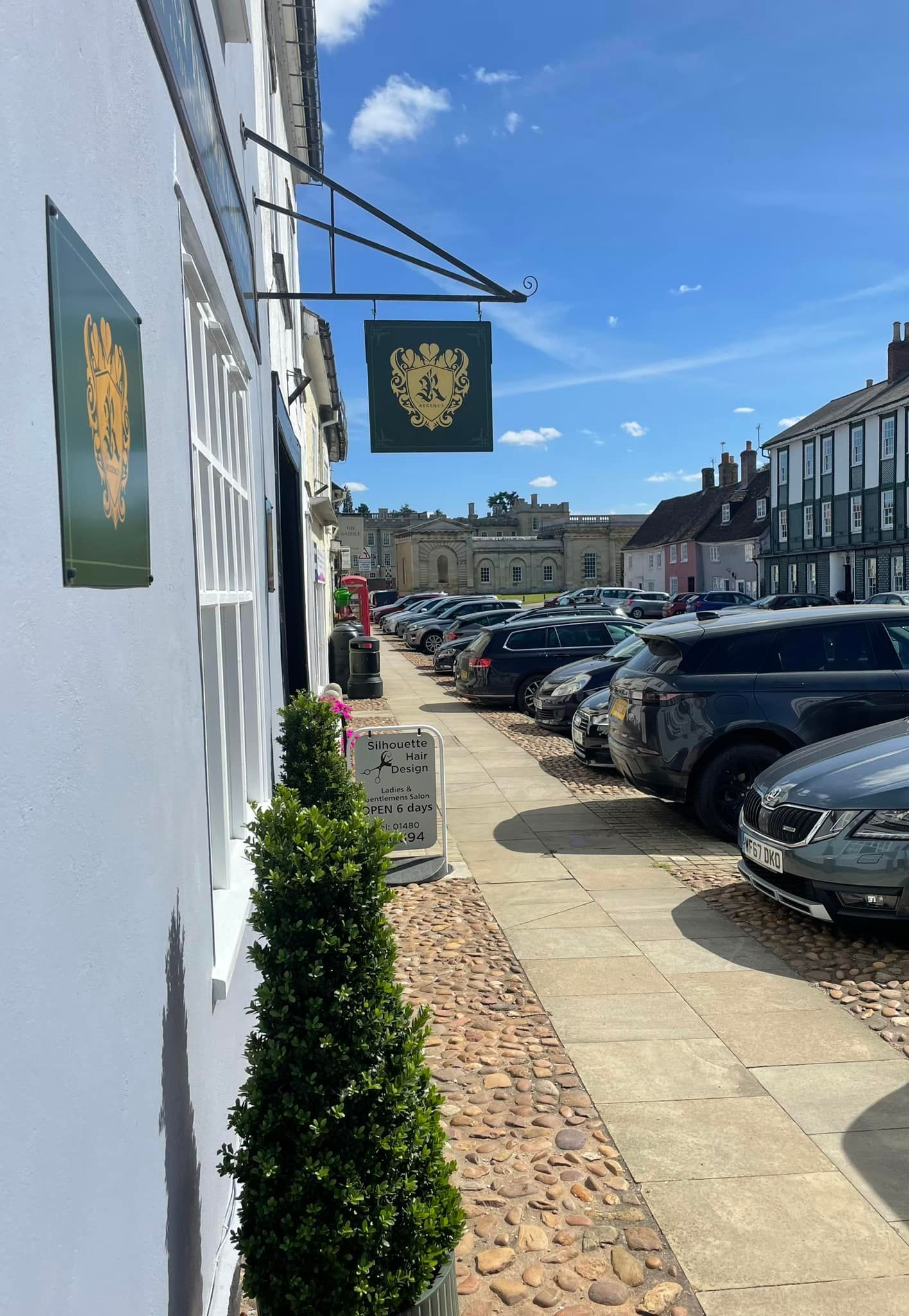 White building with sign of a skull over a road with parked cars, blue sky.
