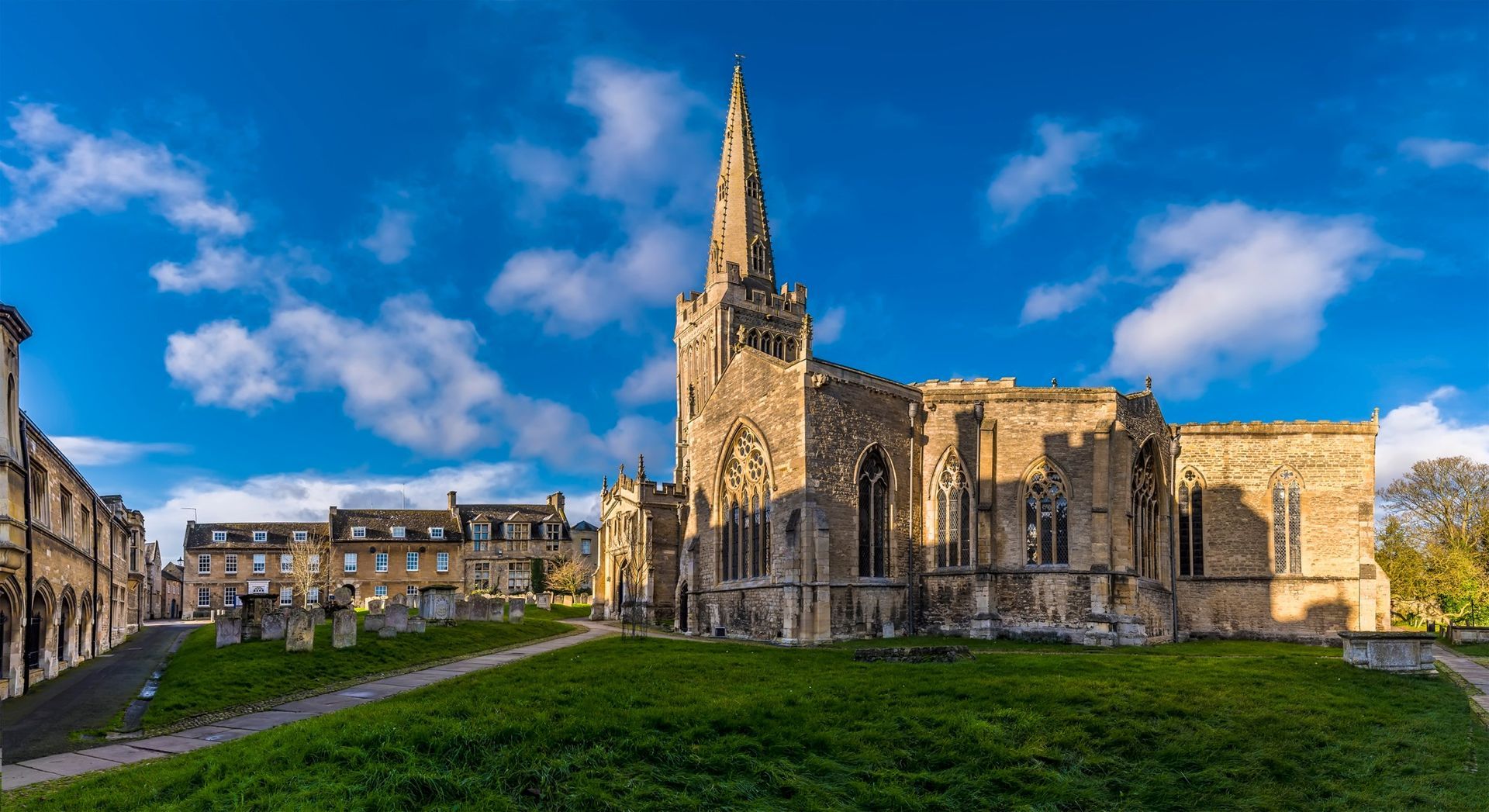 Stone church with tall spire on a grassy hill, blue sky with clouds.
