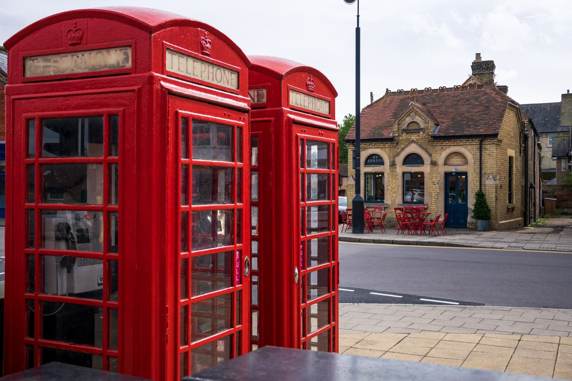 Red telephone booths stand on a sidewalk; a yellow building is in the background.