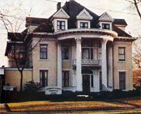 A large house with a porch and columns is sitting on top of a lush green lawn.