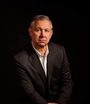 Studio portrait of a man in a dark suit against a black background, looking at the camera.