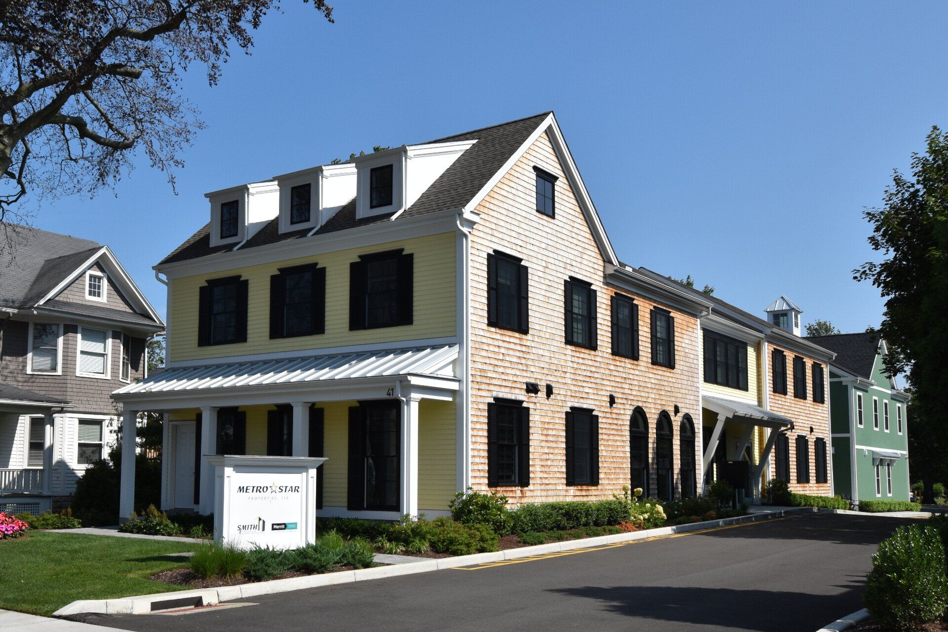 A yellow house with black shutters is next to a white house