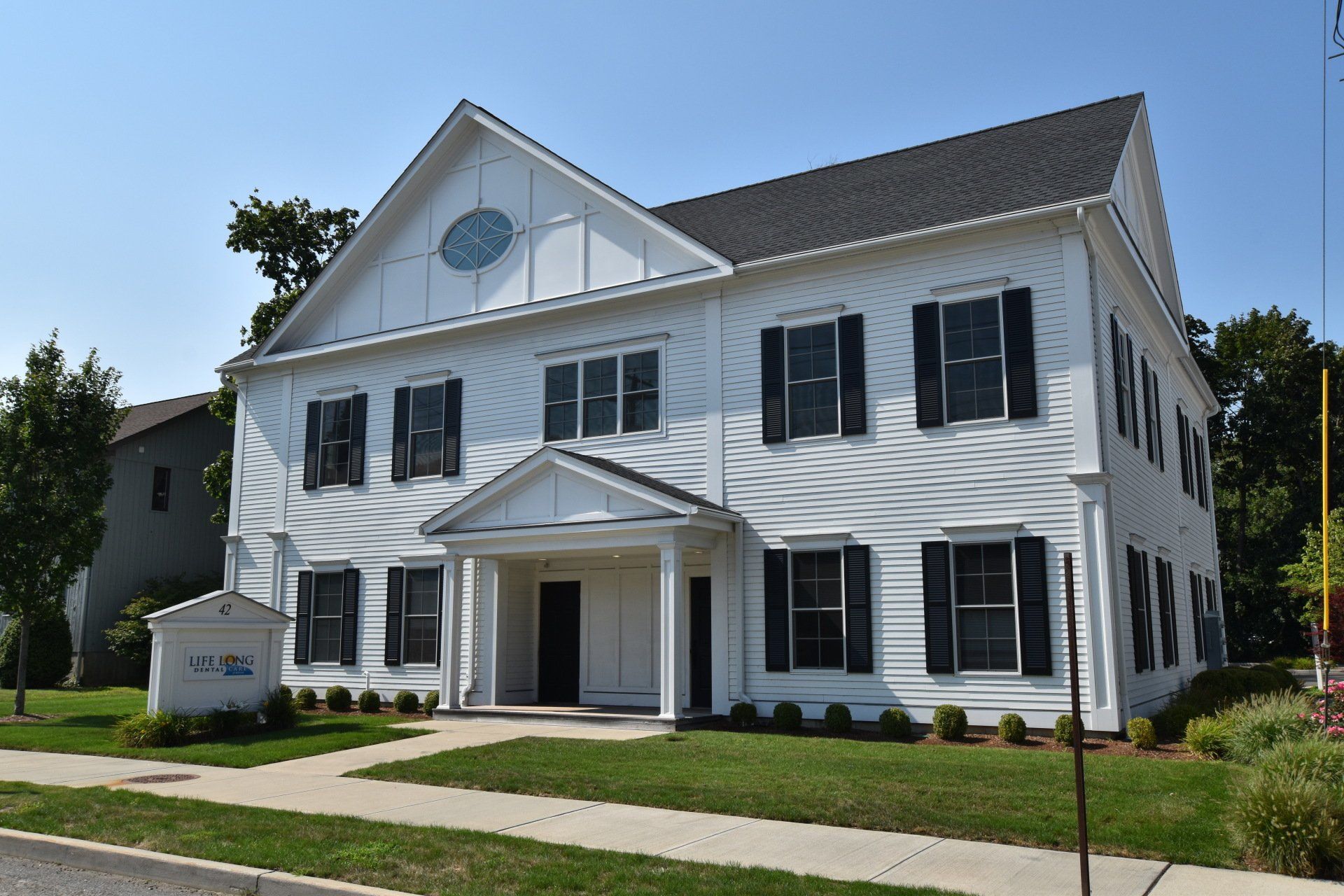 A large white house with black shutters is sitting on a lush green lawn.