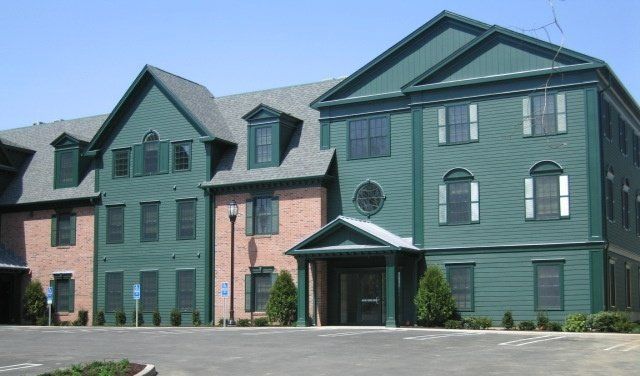 A green and brick building with a parking lot in front of it