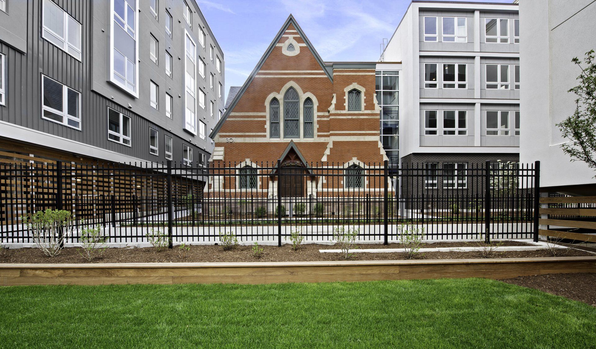 A brick church is surrounded by a fence and a row of buildings.