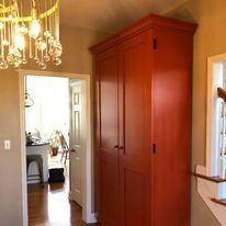 A red cabinet is in a hallway next to a staircase.