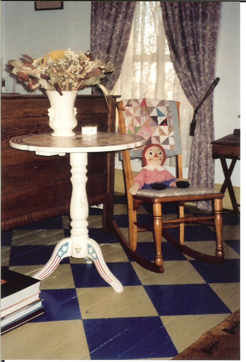 A room with a rocking chair a table and a vase of flowers