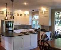 A kitchen with white cabinets , black counter tops , stainless steel appliances and a large island.