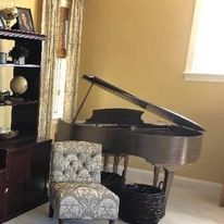 A living room with a grand piano , chair and ottoman.