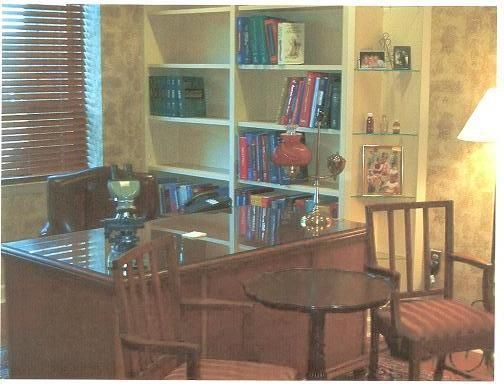 A room with a desk a chair a table and shelves full of books