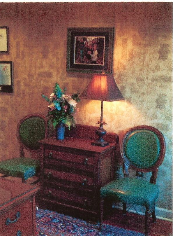 A room with two chairs a lamp and a dresser