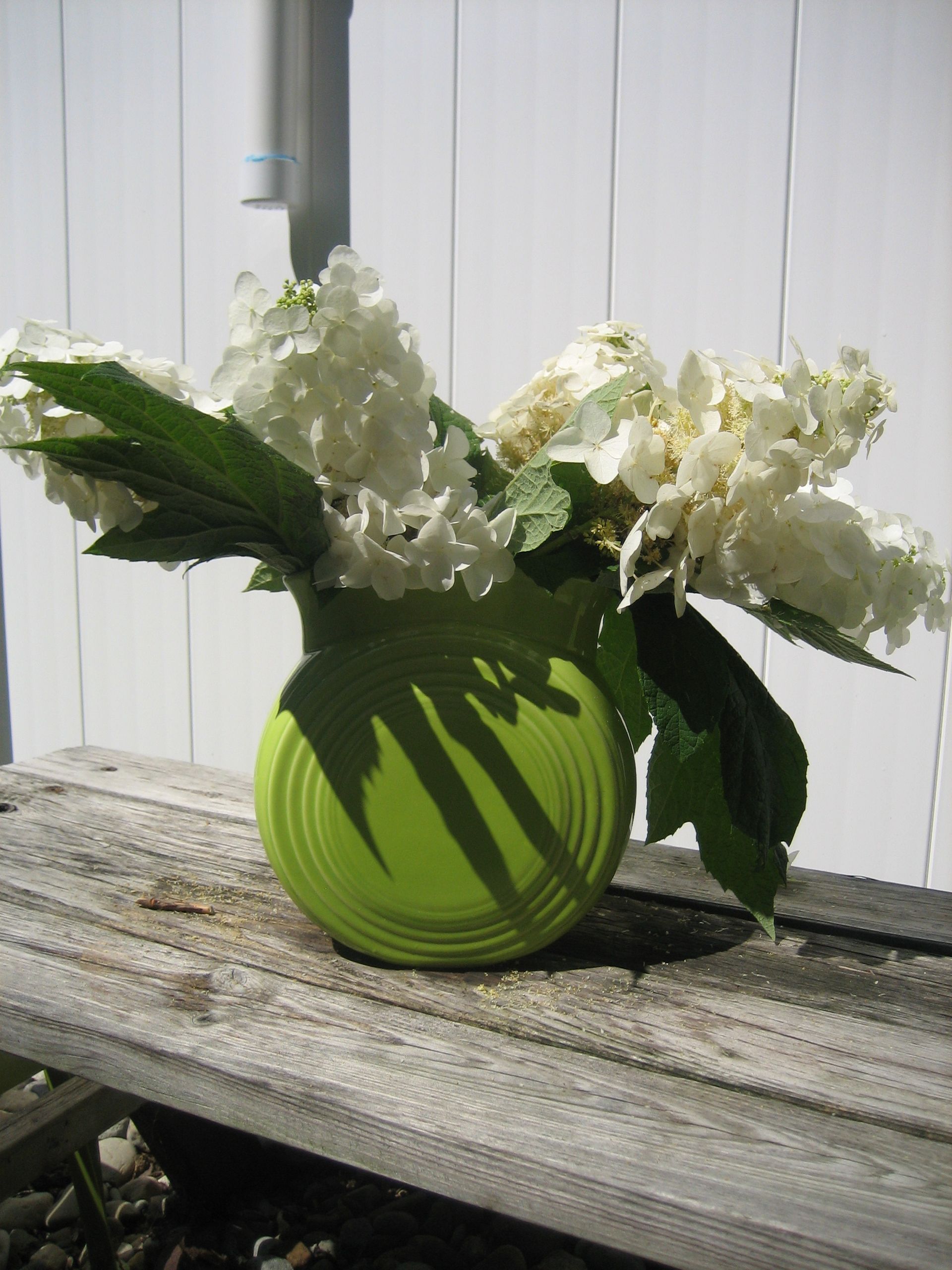 A green vase filled with white flowers sits on a wooden table